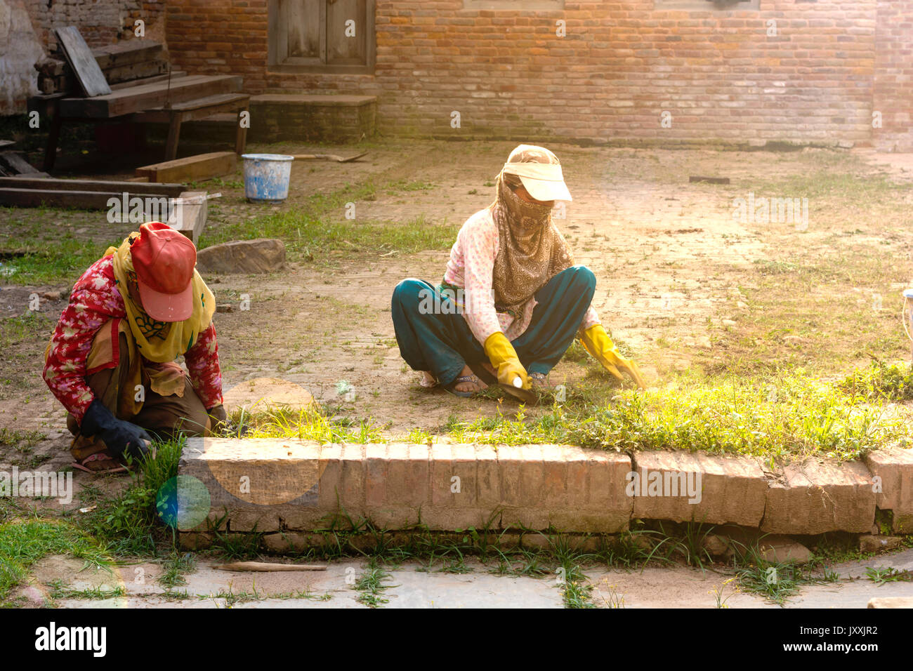 Due signore indossando tappi il taglio di erba di prato per la manutenzione del villaggio Foto Stock