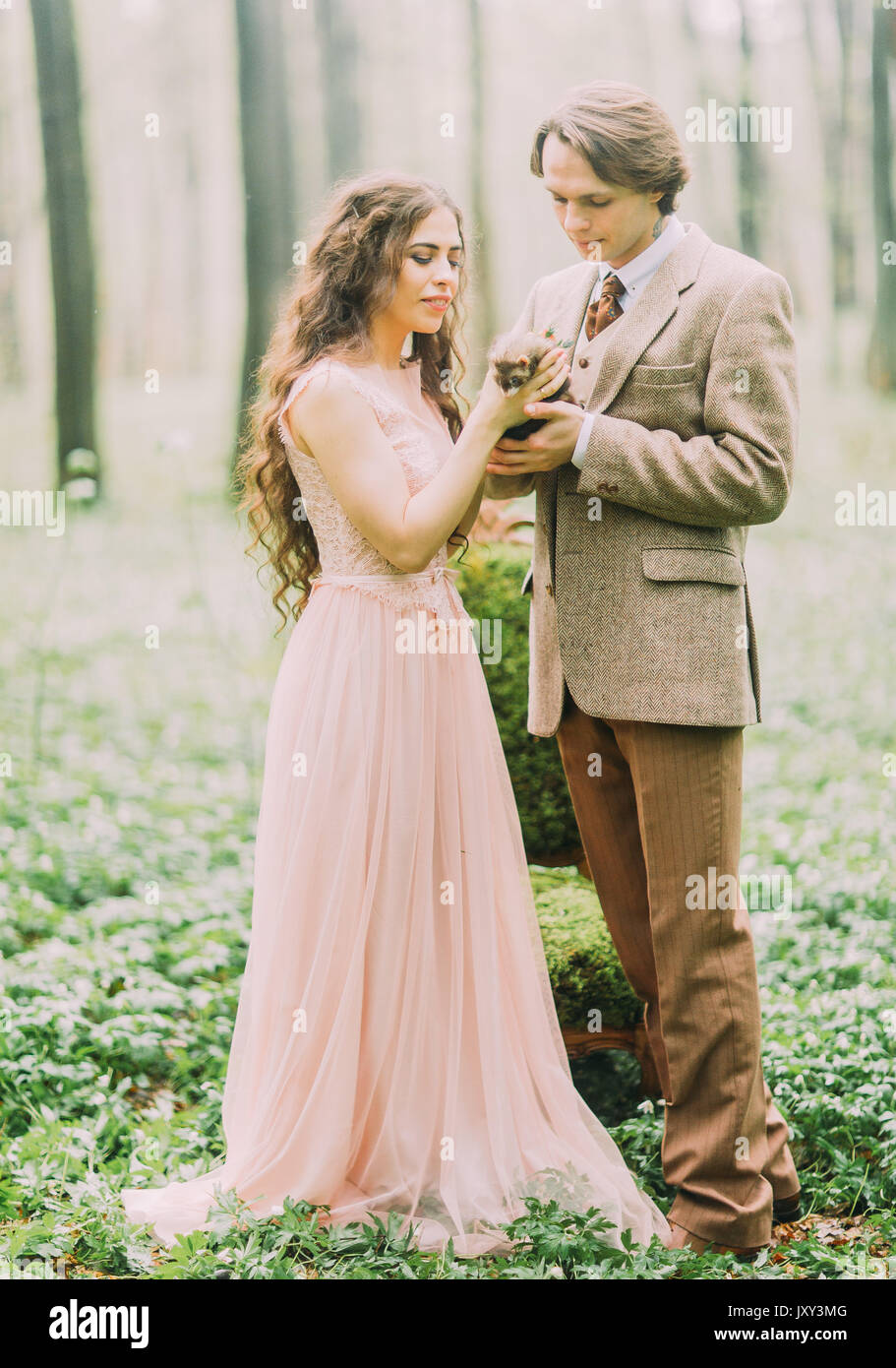 Il full-lenght foto del vintage vestito tenendo lo sposo e la sposa con lunghi capelli ricci sono holding e coccolare il marrone ferret. Foto Stock