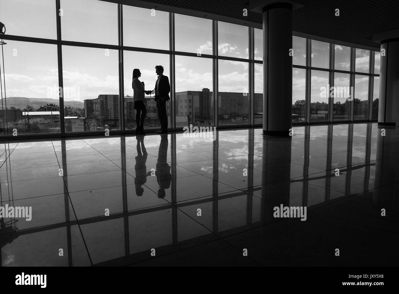 Imprenditore e imprenditrice stringono le mani in ufficio con grandi finestre panoramiche Foto Stock