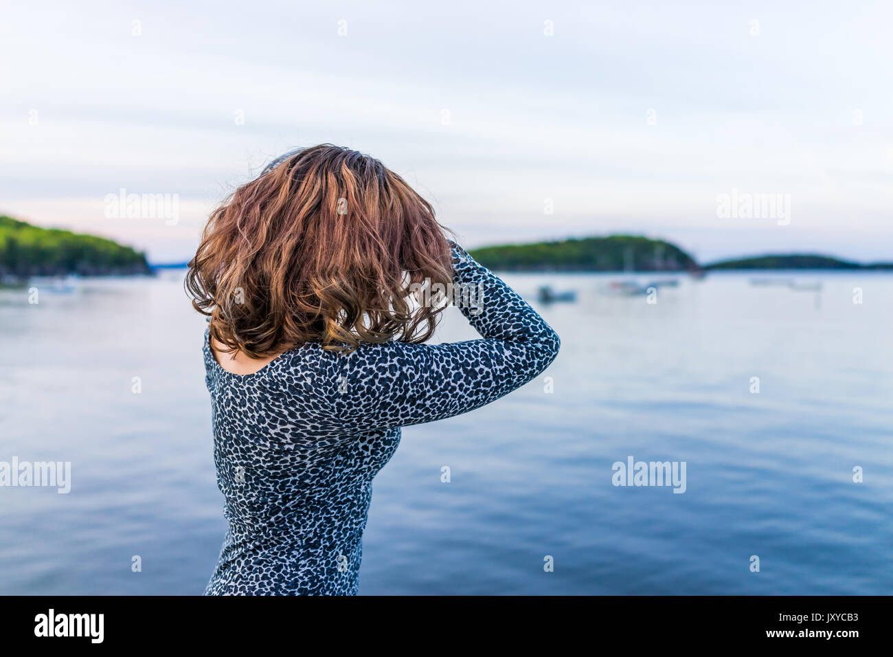 Giovane donna con le mani sulla testa sotto i capelli che si affaccia Bar Harbor, Maine bay Foto Stock