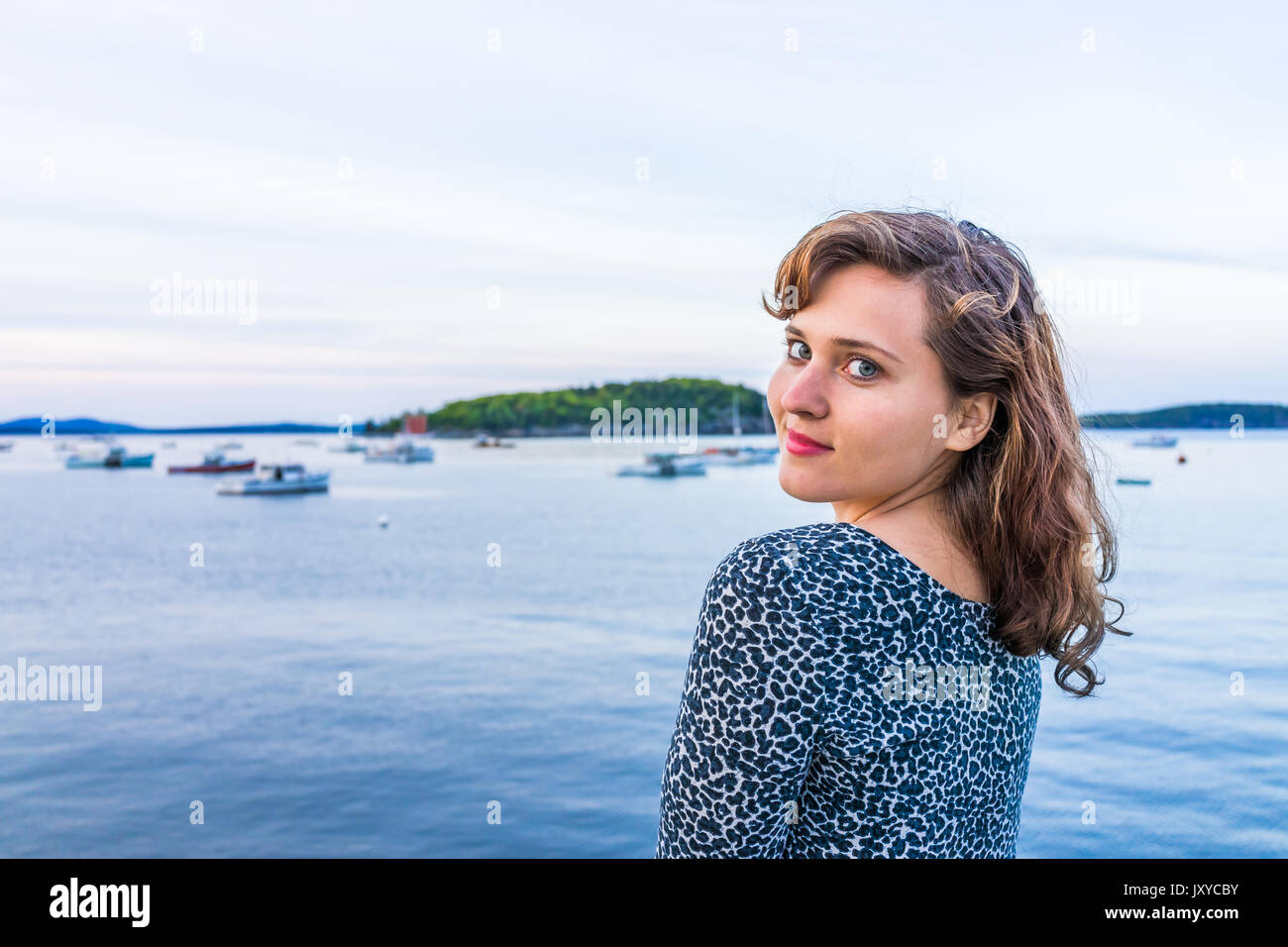 Giovani sorridenti donna seduta sul bordo del dock in Bar Harbor, Maine guardando sopra la spalla Foto Stock