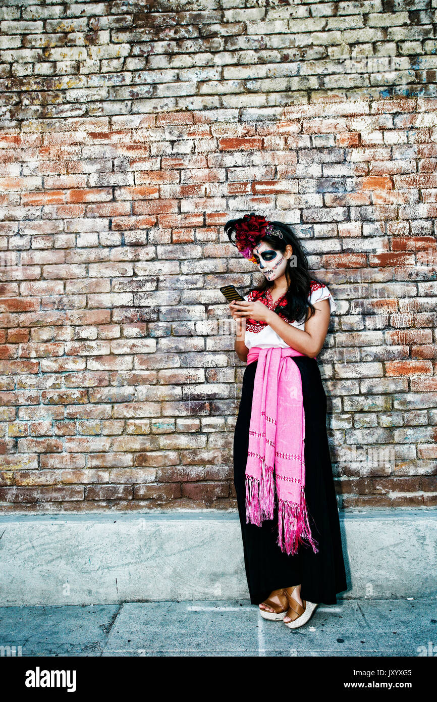 Razza mista donna sul marciapiede che indossa il teschio di vernice faccia scrivere messaggi su telefono cellulare Foto Stock