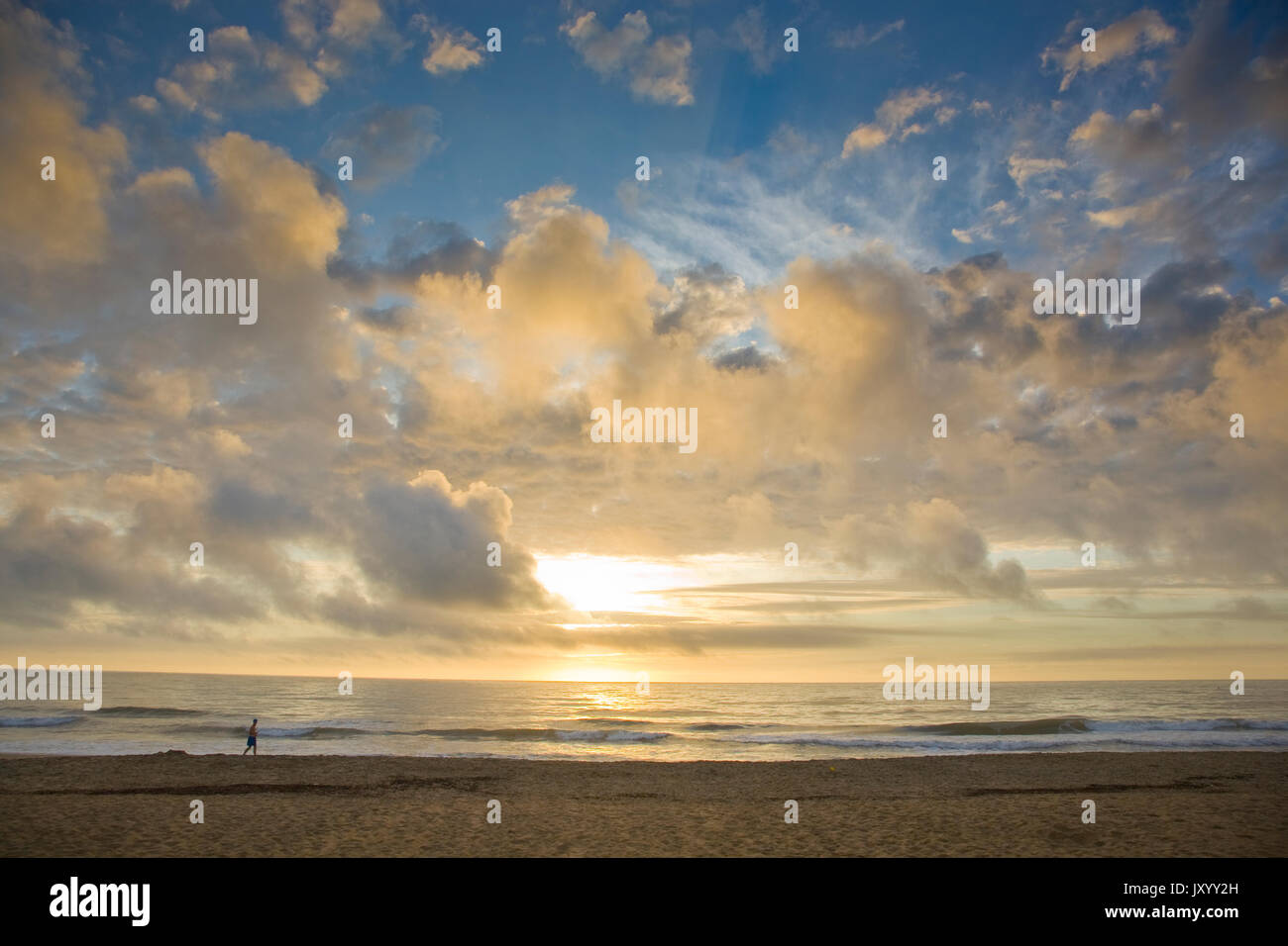 Distante uomo a camminare sulla spiaggia al tramonto Foto Stock