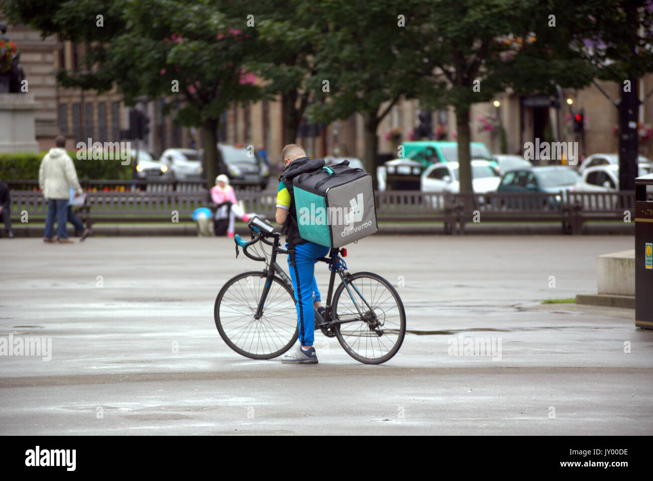 Wet george square glasgow giovane ragazzo consegna bike ciclista deliveroo Consegna del cibo scrivere messaggi in attesa per il lavoro offrendo al di fuori sulla strada Foto Stock