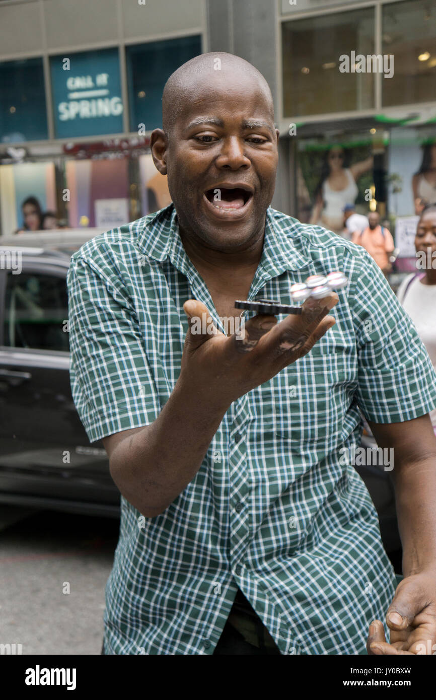 Un espressivo uomo vendere filatori agitano: dimostra la filatura alcuni di loro in uno. In Herald Square sezione di Manhattan, New York City. Foto Stock