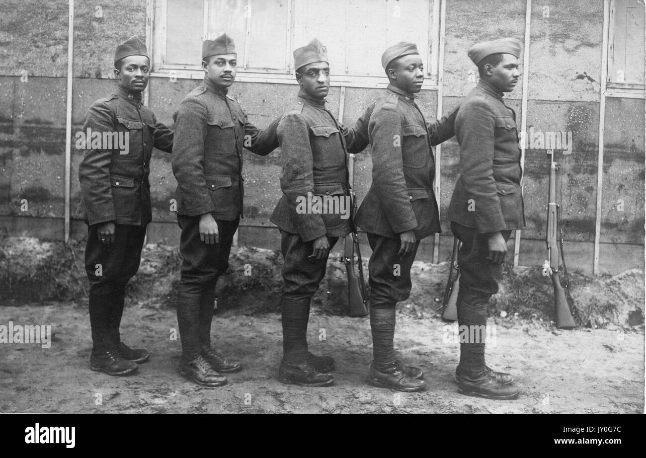 Ritratto di gruppo di cinque soldati afro-americani con espressioni neutre in uniforme all'esterno di un edificio, le loro armi poggiano contro il suo fianco, 1920. Foto Stock