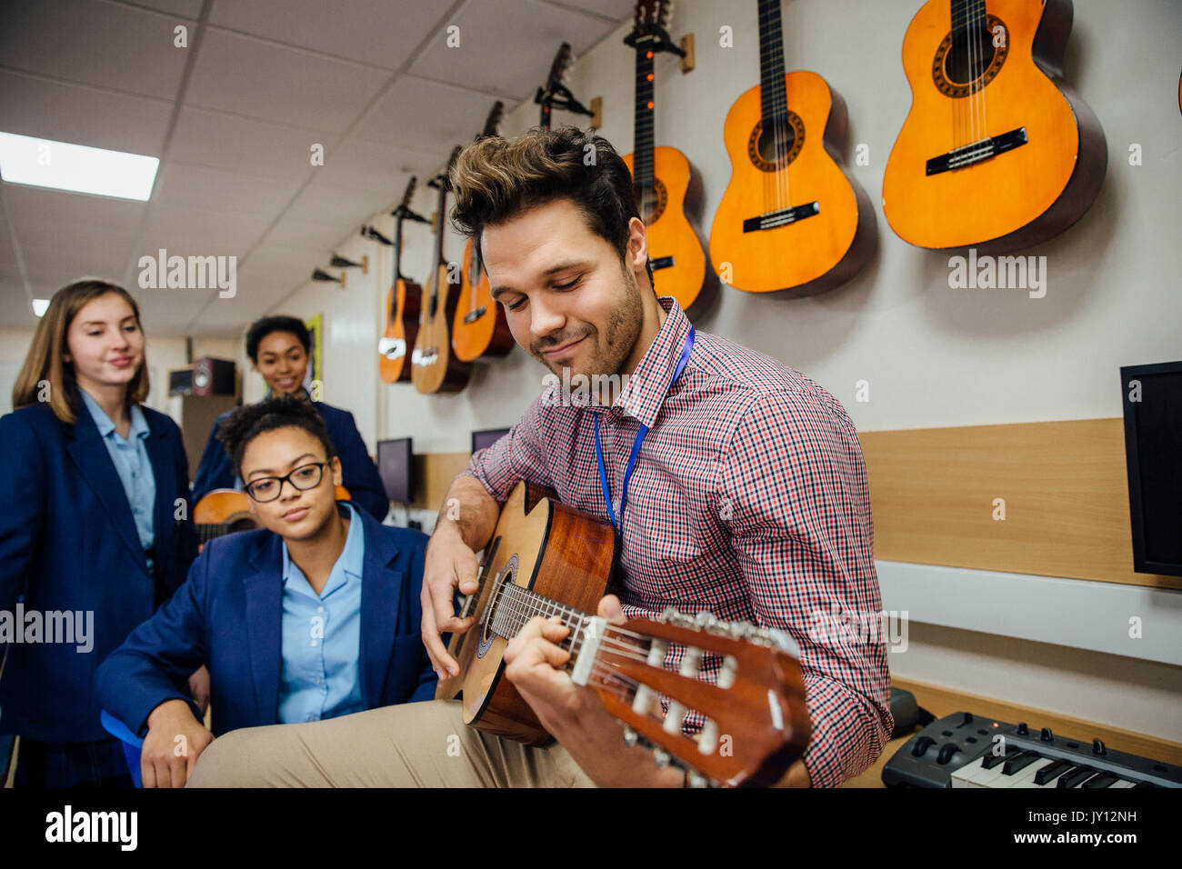 Insegnante di sesso maschile è di suonare una chitarra nella sua lezione di  musica e i suoi studenti stanno a guardare Foto stock - Alamy