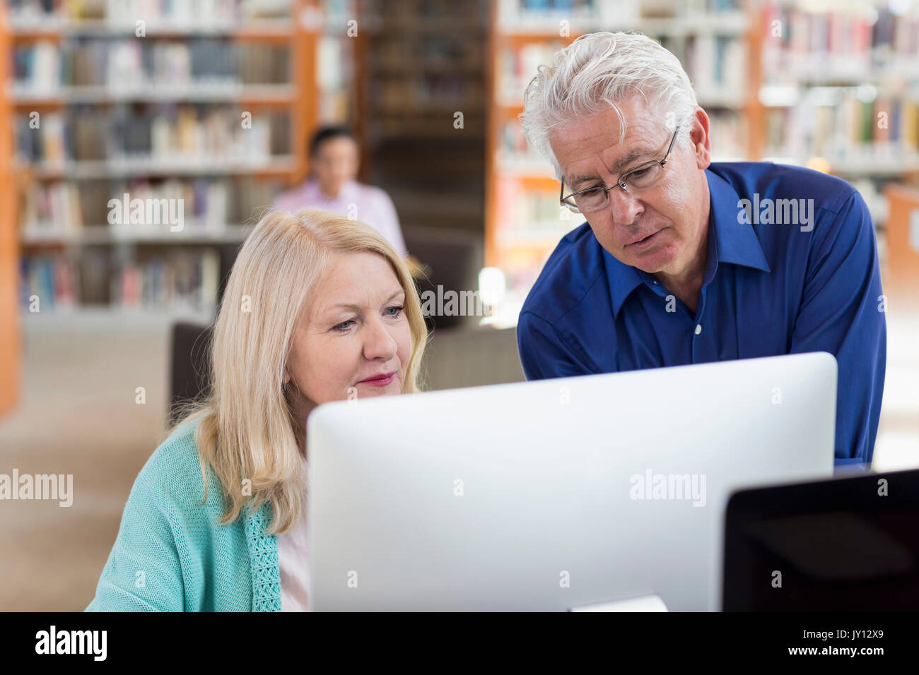 Vecchio Uomo Donna aiuta a utilizzare il computer nella libreria Foto Stock