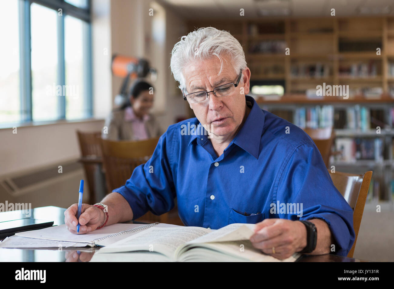 Uomo vecchio libro di lettura in biblioteca e scrivere note Foto Stock