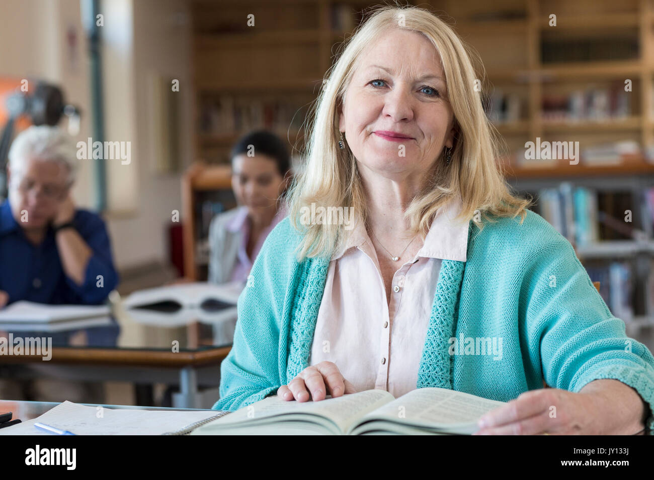 Sorridente donna anziana la lettura di libro in biblioteca Foto Stock