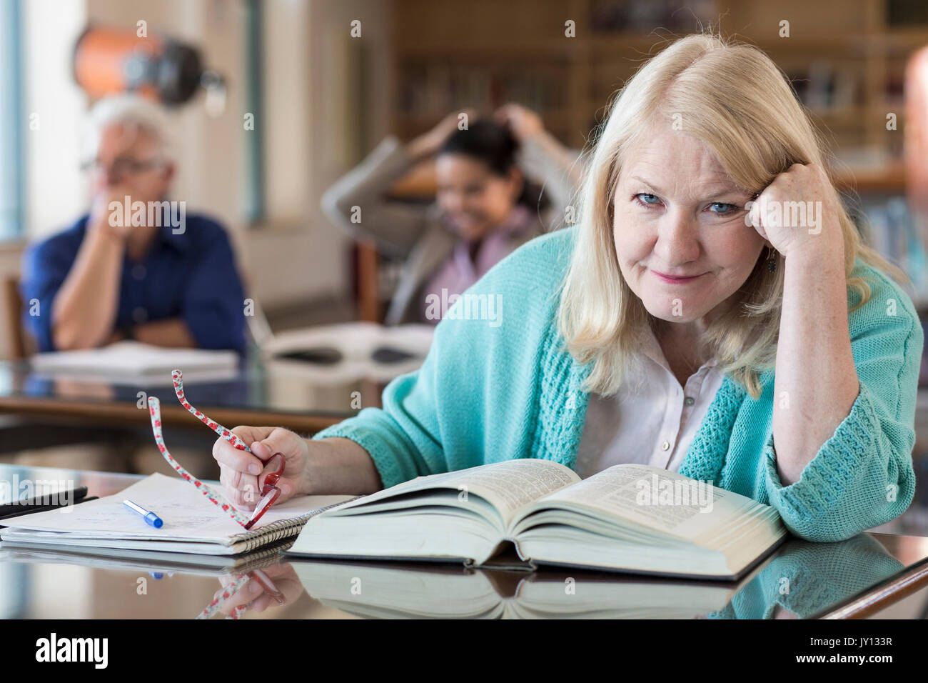 Confuso donna anziana la lettura di libro in biblioteca Foto Stock