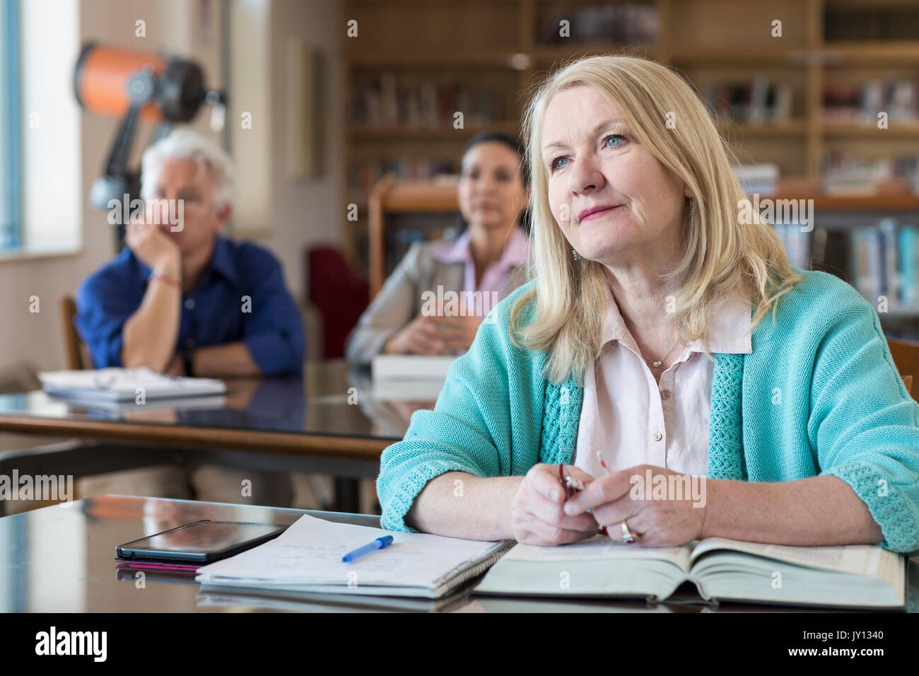 Curioso donna anziana ascolto in biblioteca Foto Stock