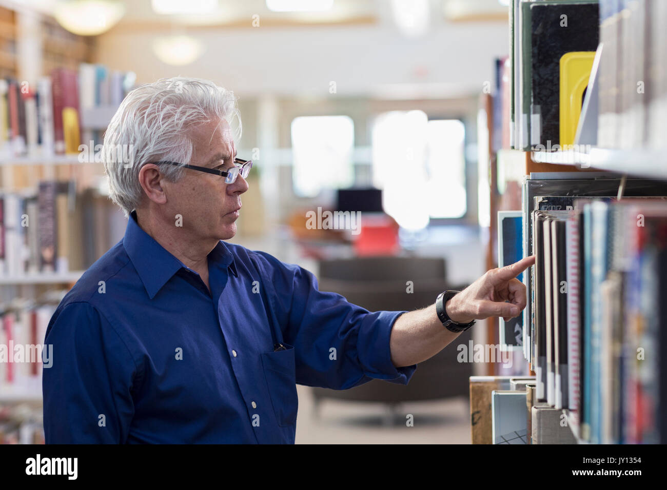 Curioso uomo ispanico ricerca di libro in biblioteca Foto Stock