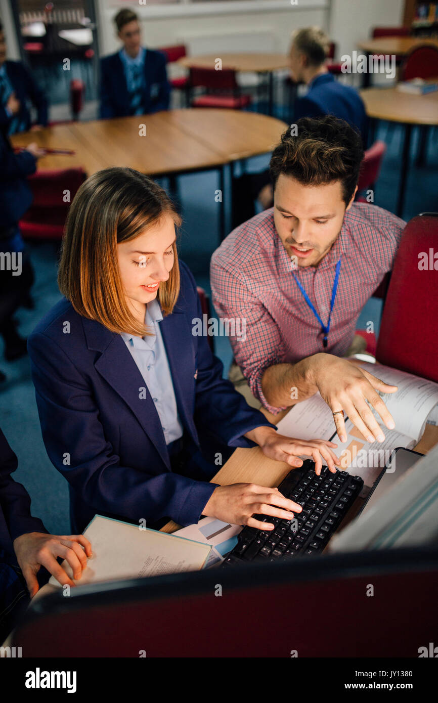 Teen studente è di essere assistiti con il suo lavoro dal suo maestro. Egli è idscussing qualcosa dal libro di testo con lei e lei è la digitazione di informazioni su Foto Stock