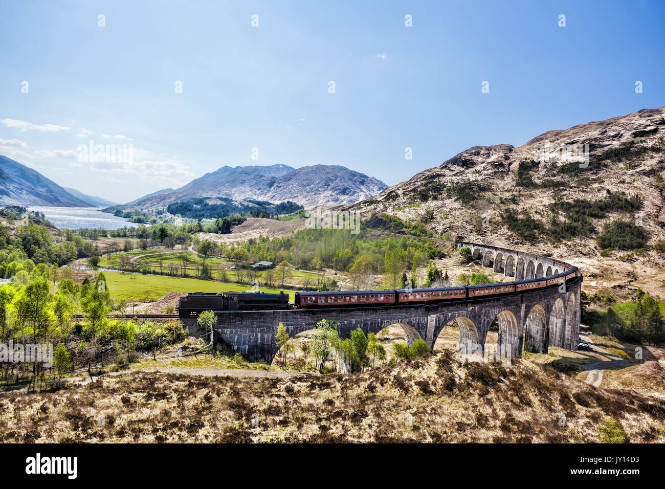 Glenfinnan viadotto ferroviario in Scozia con il vapore giacobita treno contro il tramonto sul lago Foto Stock