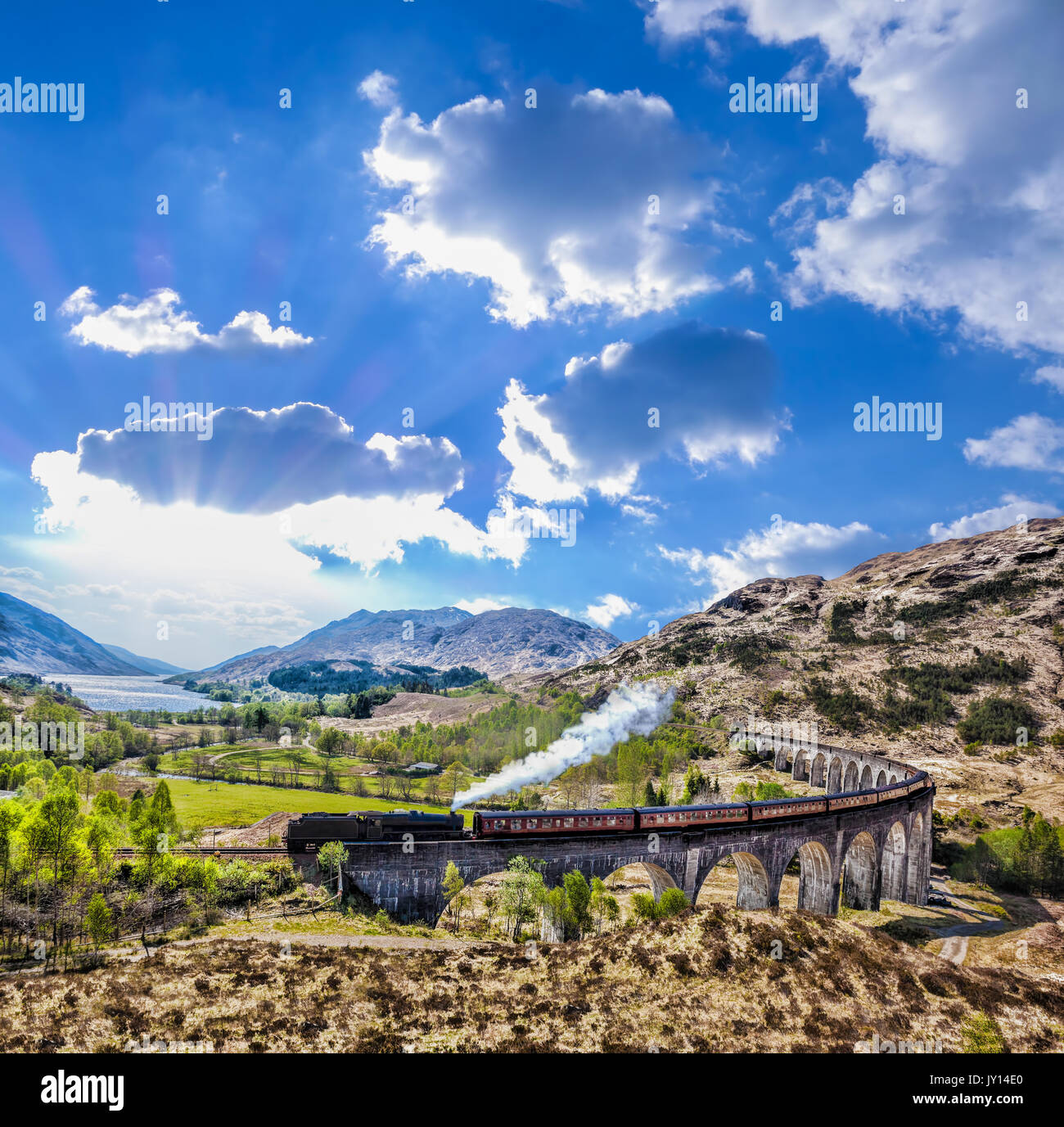 Glenfinnan viadotto ferroviario in Scozia con il vapore giacobita treno contro il tramonto sul lago Foto Stock