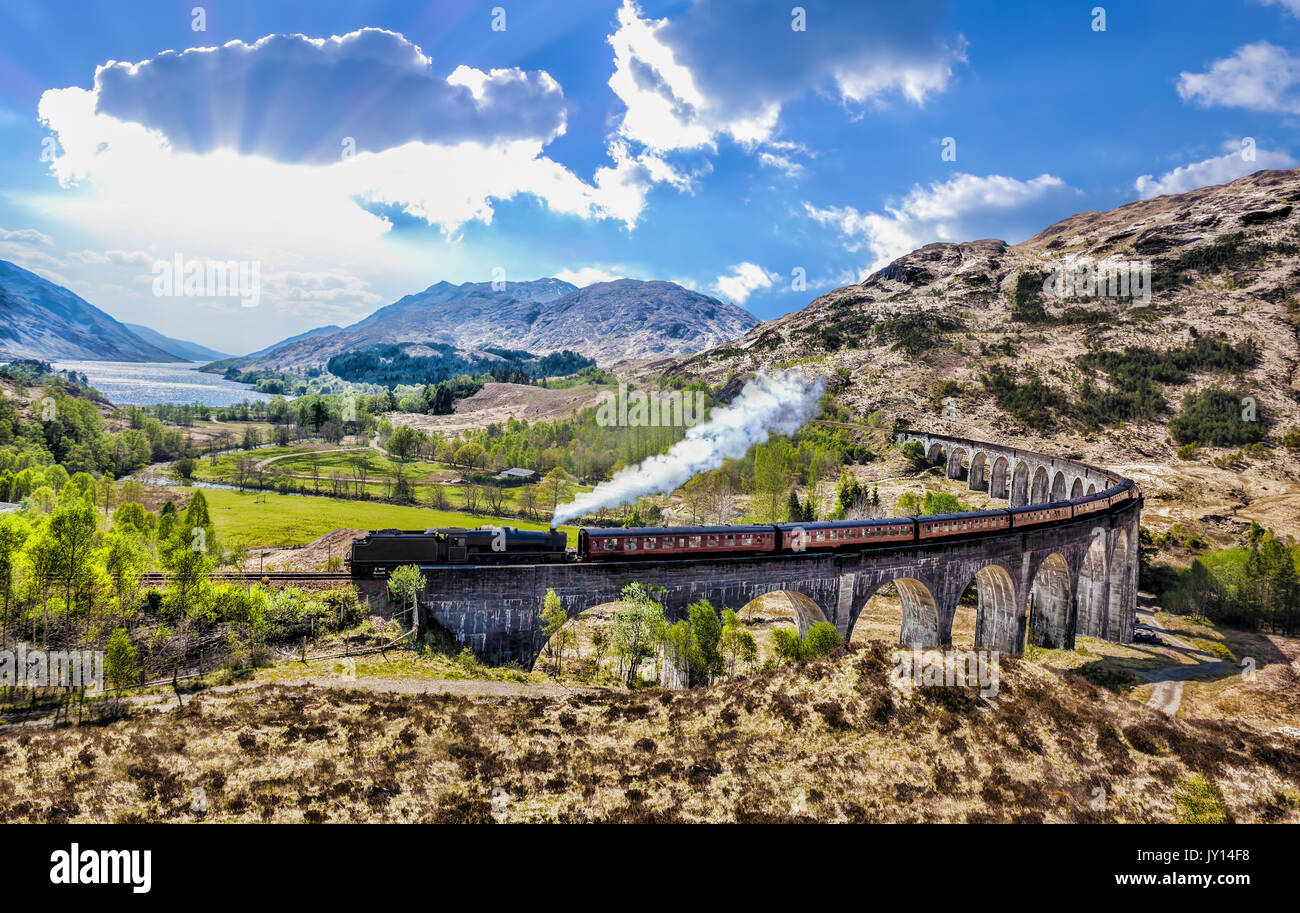 Glenfinnan viadotto ferroviario in Scozia con il vapore giacobita treno contro il tramonto sul lago Foto Stock