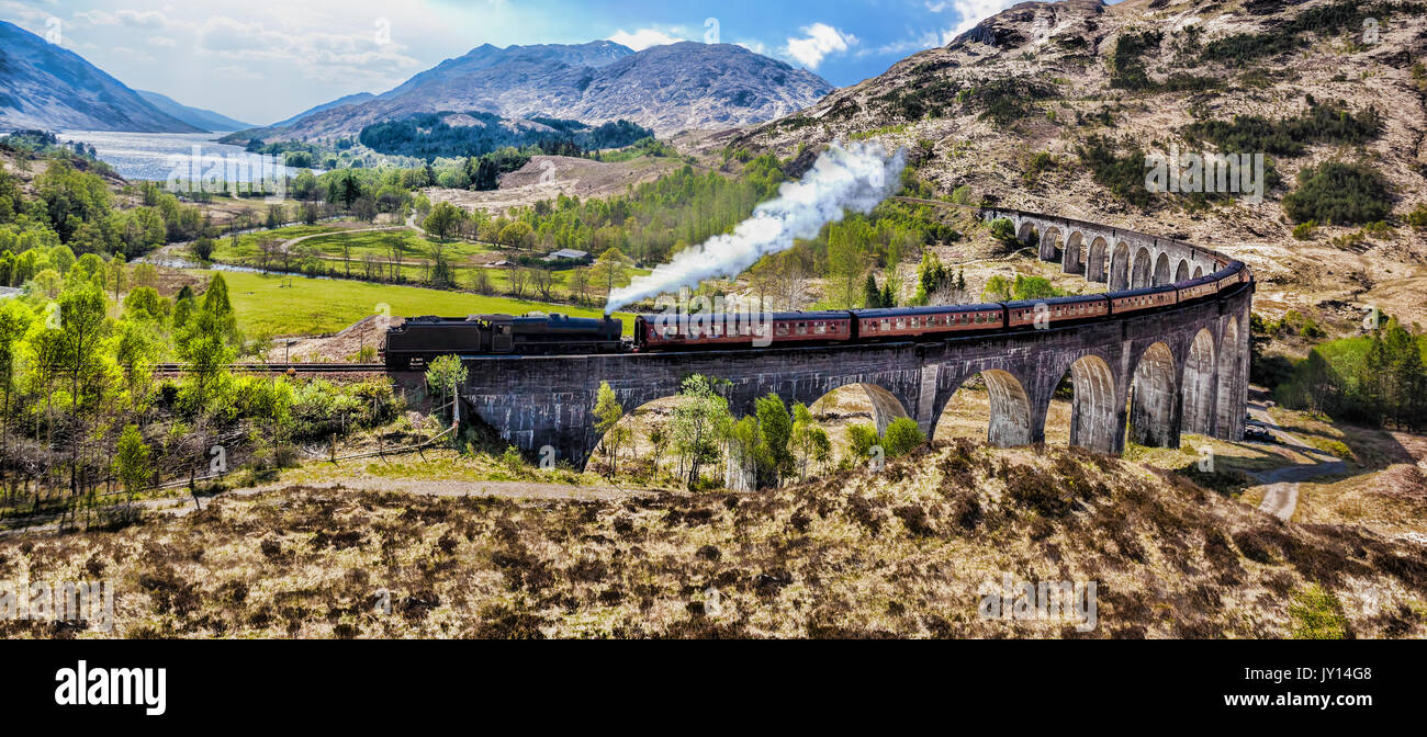 Glenfinnan viadotto ferroviario in Scozia con il vapore giacobita treno contro il tramonto sul lago Foto Stock