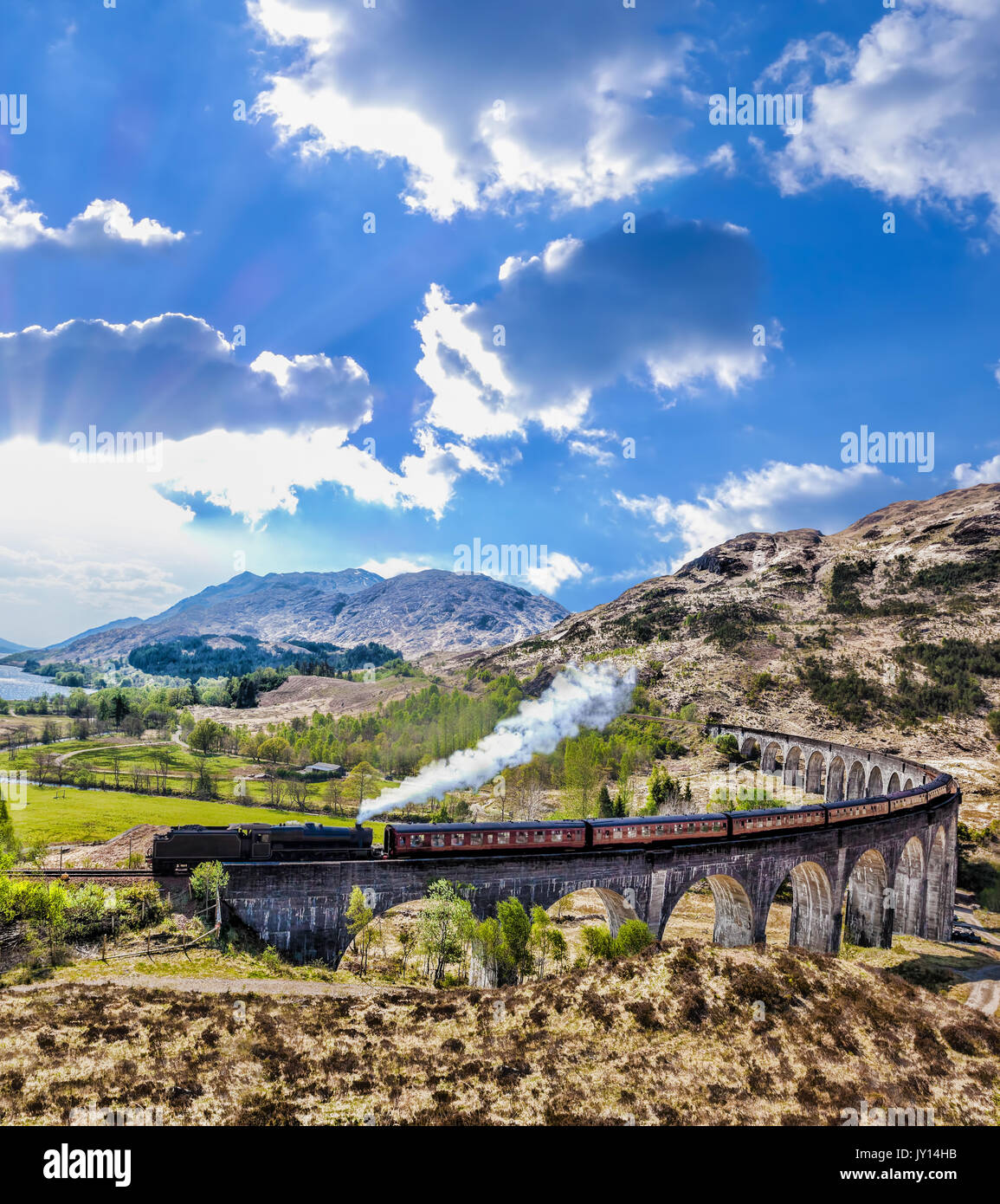 Glenfinnan viadotto ferroviario in Scozia con il vapore giacobita treno contro il tramonto sul lago Foto Stock