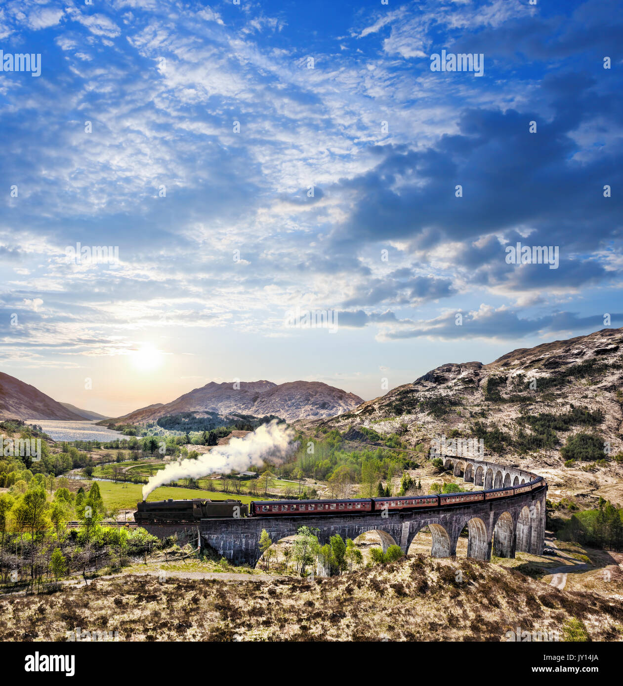 Glenfinnan viadotto ferroviario in Scozia con il vapore giacobita treno contro il tramonto sul lago Foto Stock