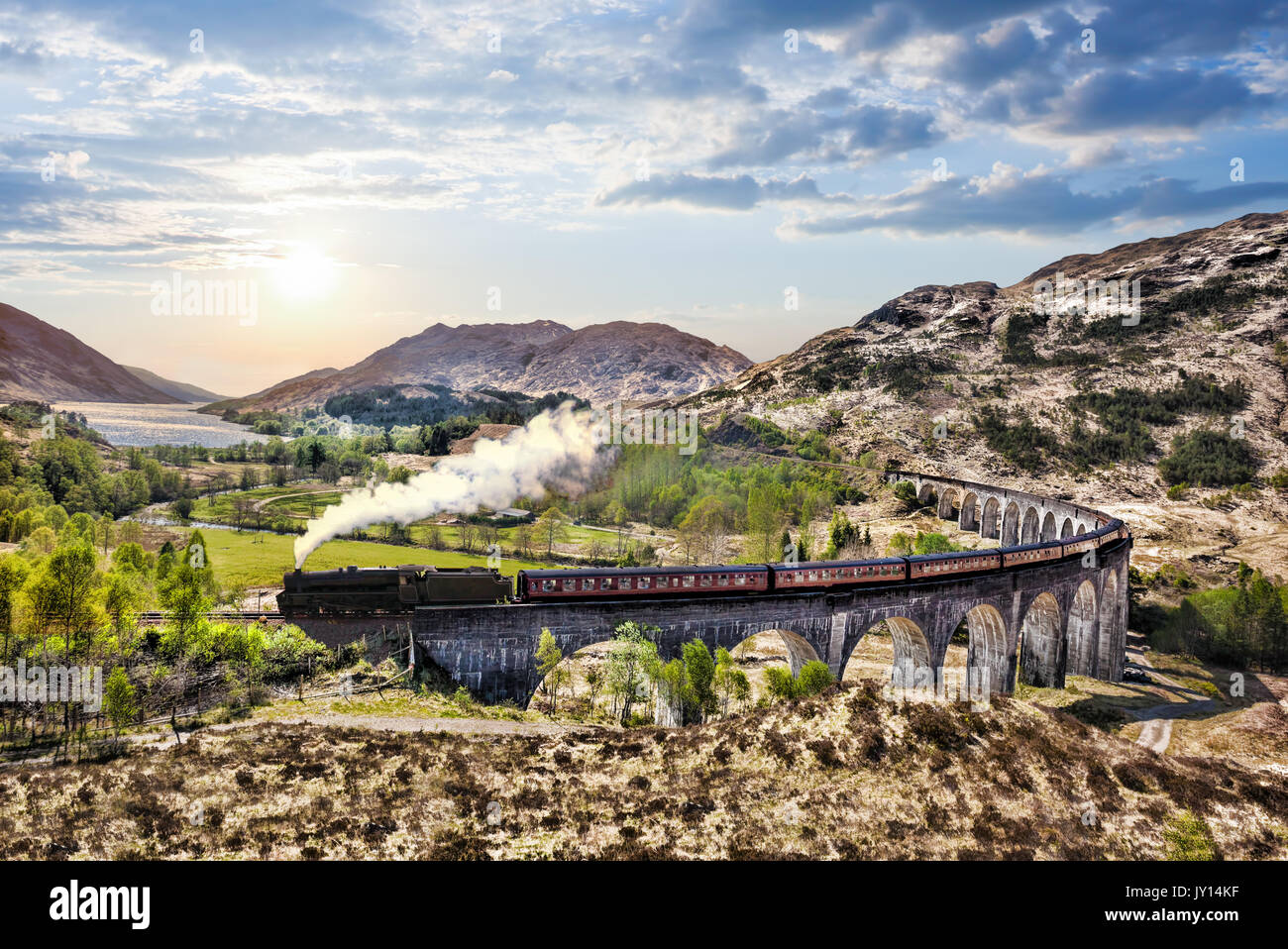 Glenfinnan viadotto ferroviario in Scozia con il vapore giacobita treno contro il tramonto sul lago Foto Stock