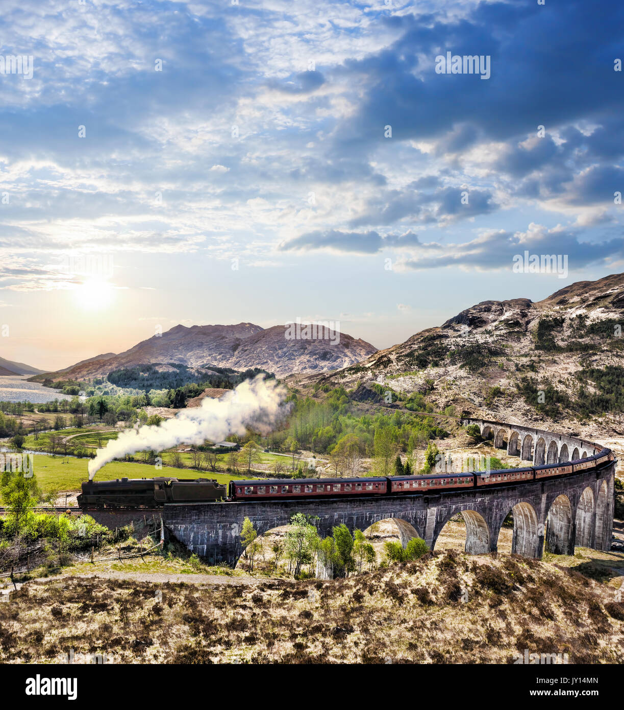 Glenfinnan viadotto ferroviario in Scozia con il vapore giacobita treno contro il tramonto sul lago Foto Stock