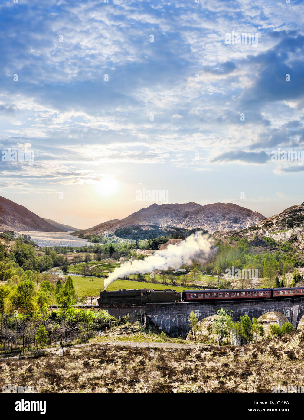 Glenfinnan viadotto ferroviario in Scozia con il vapore giacobita treno contro il tramonto sul lago Foto Stock