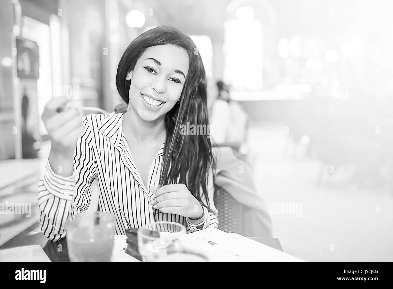 Bruna giovane donna con capelli lunghi cercando di fotocamera e sorridere mentre mangiando cioccolato torta nella caffetteria. Foto Stock