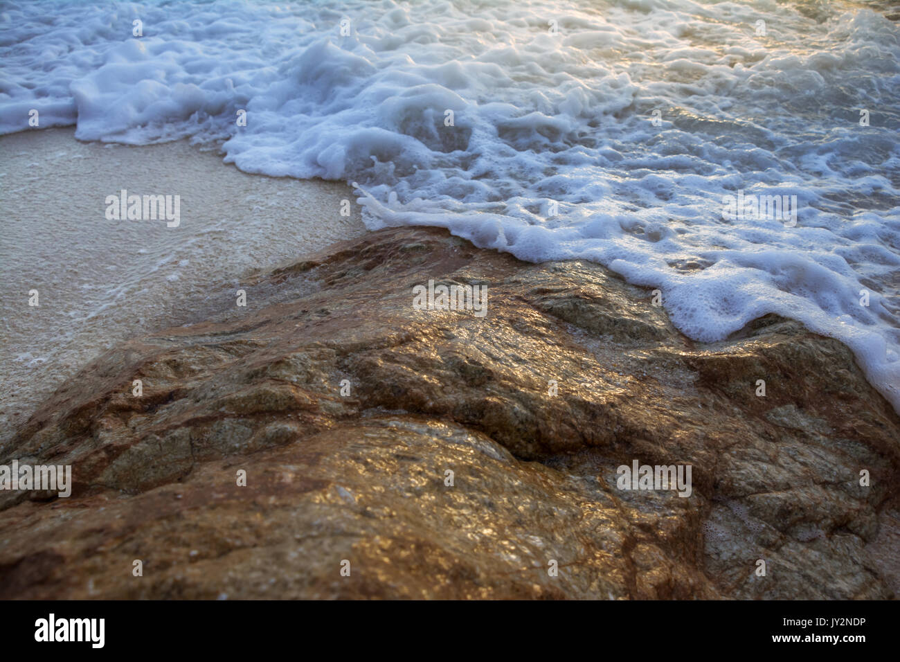 Morbide onde colpire le rocce con la luce solare Foto Stock