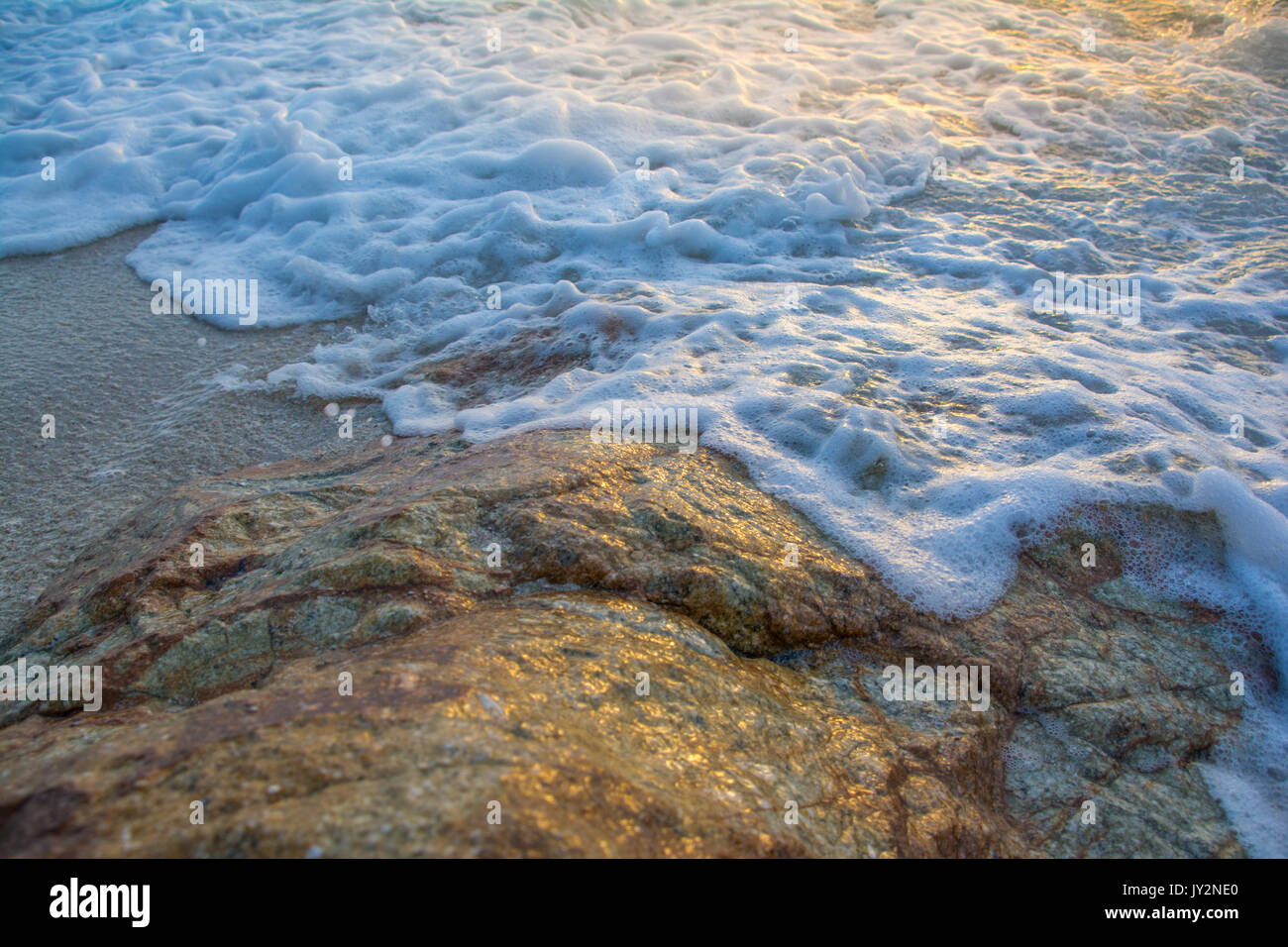 Morbide onde colpire le rocce con la luce solare Foto Stock