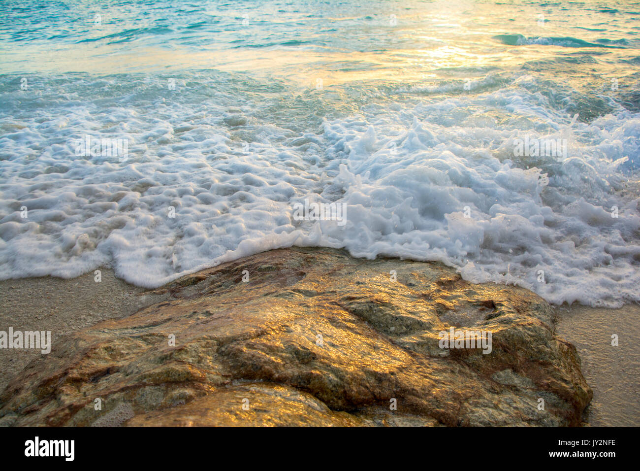 Morbide onde colpire le rocce con la luce solare Foto Stock