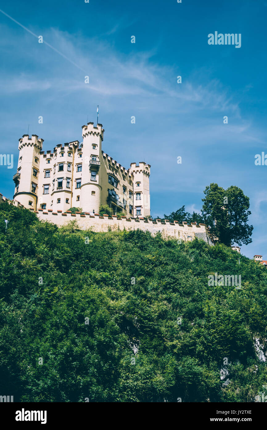 Il castello di Hohenschwangau su una collina con un cielo blu visto dal di sotto. Foto Stock