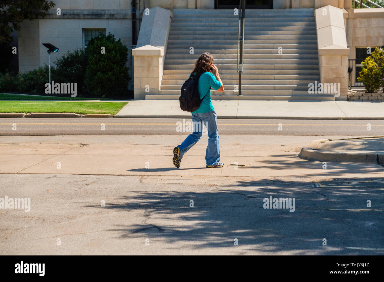 Un giovane maschio studente di college con zaino sul suo telefono cellulare mentre si cammina alla classe in Norman Oklahoma, casa dell'Università di Oklahoma, Oklahoma, Foto Stock