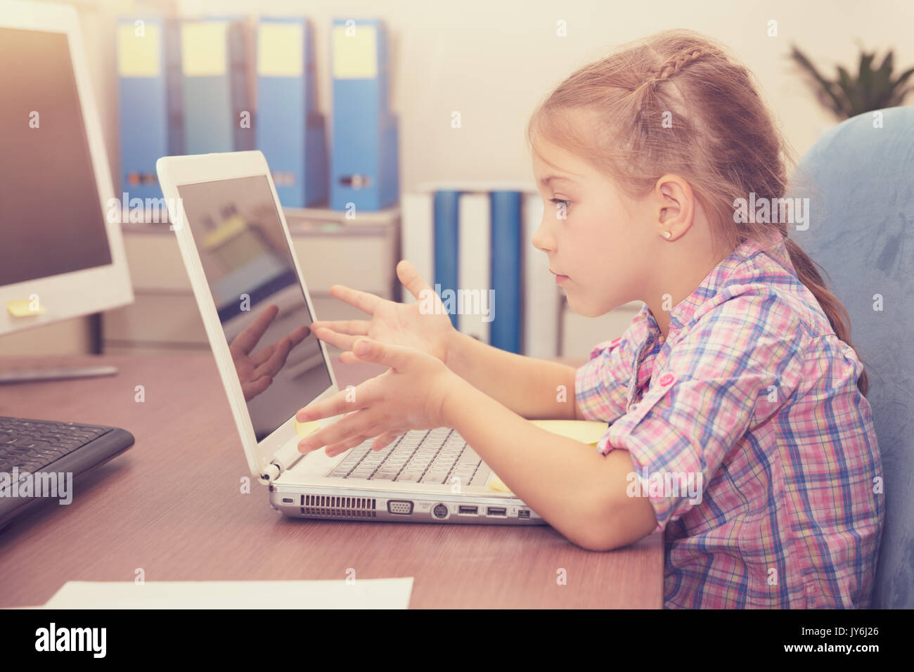 Bambina facendo i compiti sul computer portatile, istruzione a casa, emotivamente con gesti risoluzione difficile compito, moderno processo educativo di un litt Foto Stock