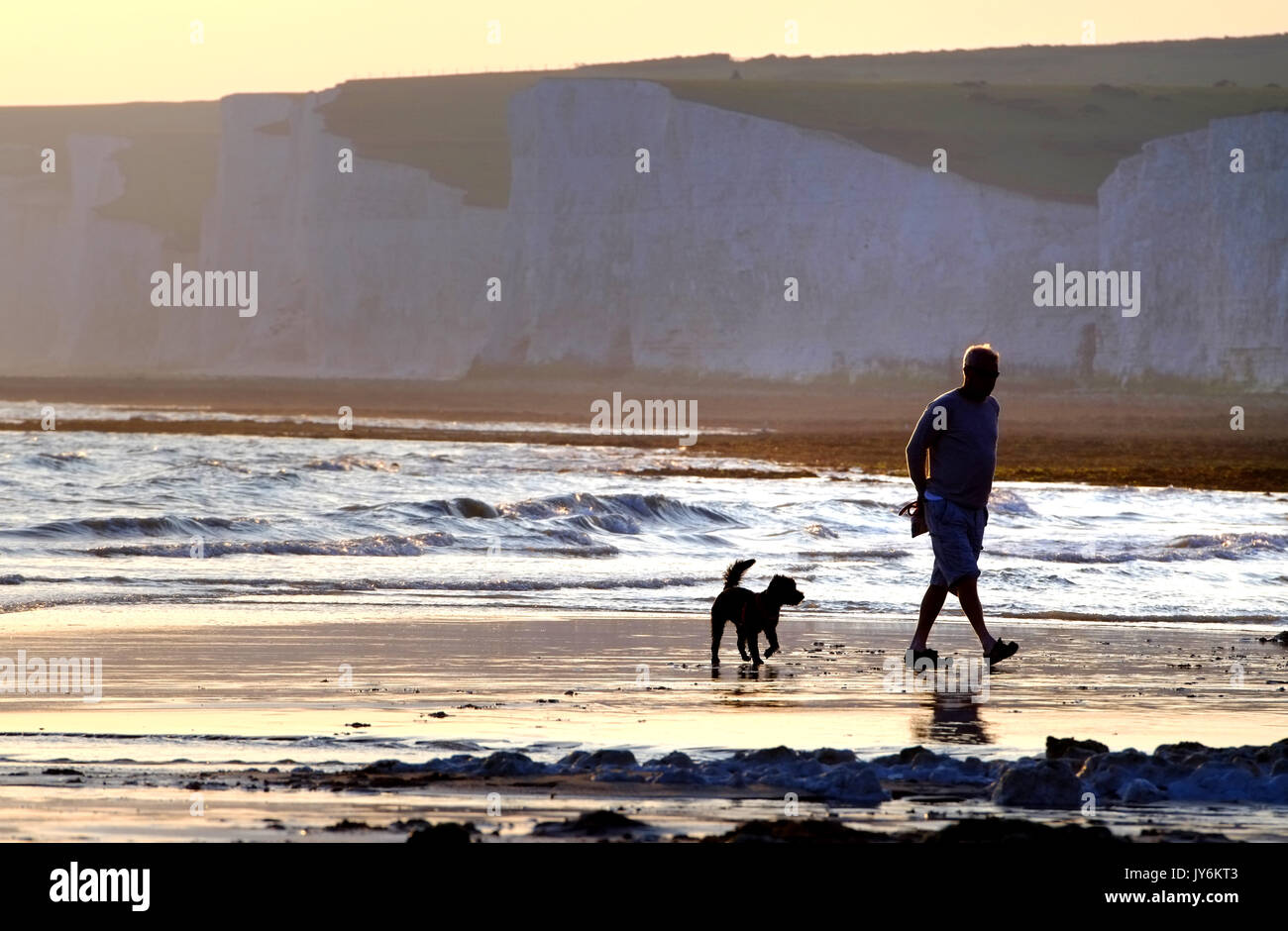 L uomo e il suo cane a camminare sulla spiaggia vicino la mitica sette sorelle chalk cliffs, East Sussex. Foto Stock