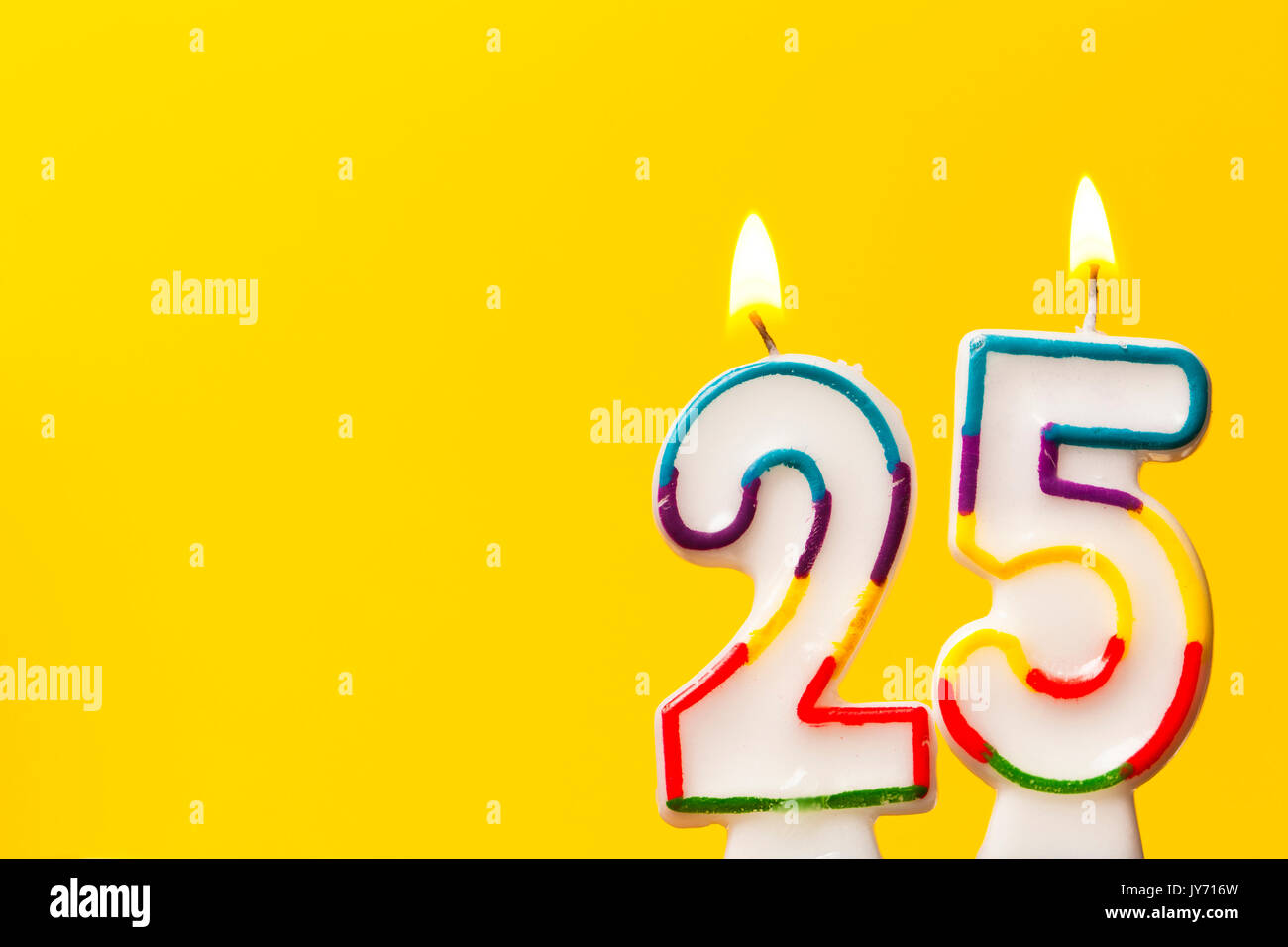 Numero 25 celebrazione di compleanno candela contro un luminoso sfondo giallo Foto Stock