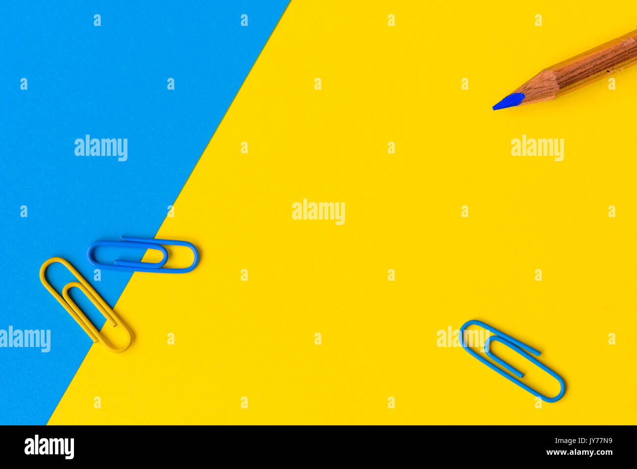 Una matita di legno con una punta blu e tre graffette contro un blu e sfondo giallo con copia spazio. Foto Stock