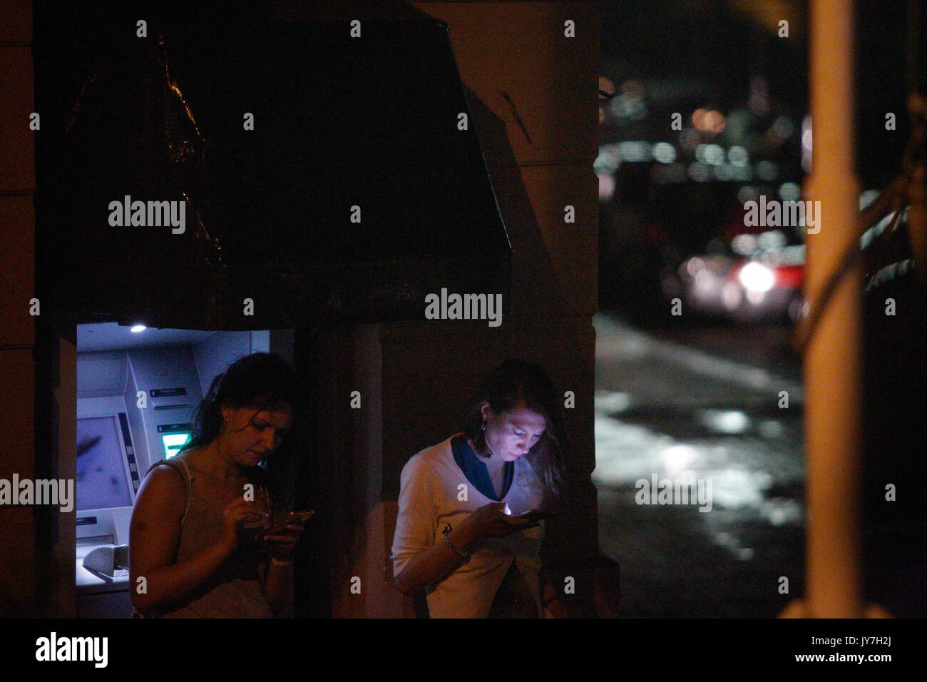 Due donne sono visti utilizzando i loro telefoni cellulari tenendo il coperchio dalla pioggia nei pressi di un ATM nel centro della città su 11 Agosto, 2017. Foto Stock
