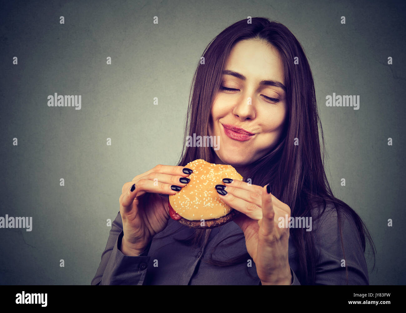 Donna mangiare un Big hamburger, isolata su uno sfondo grigio Foto Stock