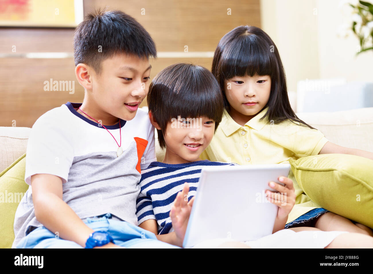 Tre asiatico i bambini seduti sul divano a casa la riproduzione del video gioco utilizzando digitale compressa. Foto Stock
