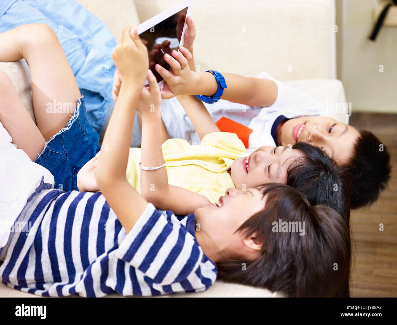 Tre bambini asiatici sdraiato sul lettino a casa la riproduzione del video gioco utilizzando digitale compressa. Foto Stock