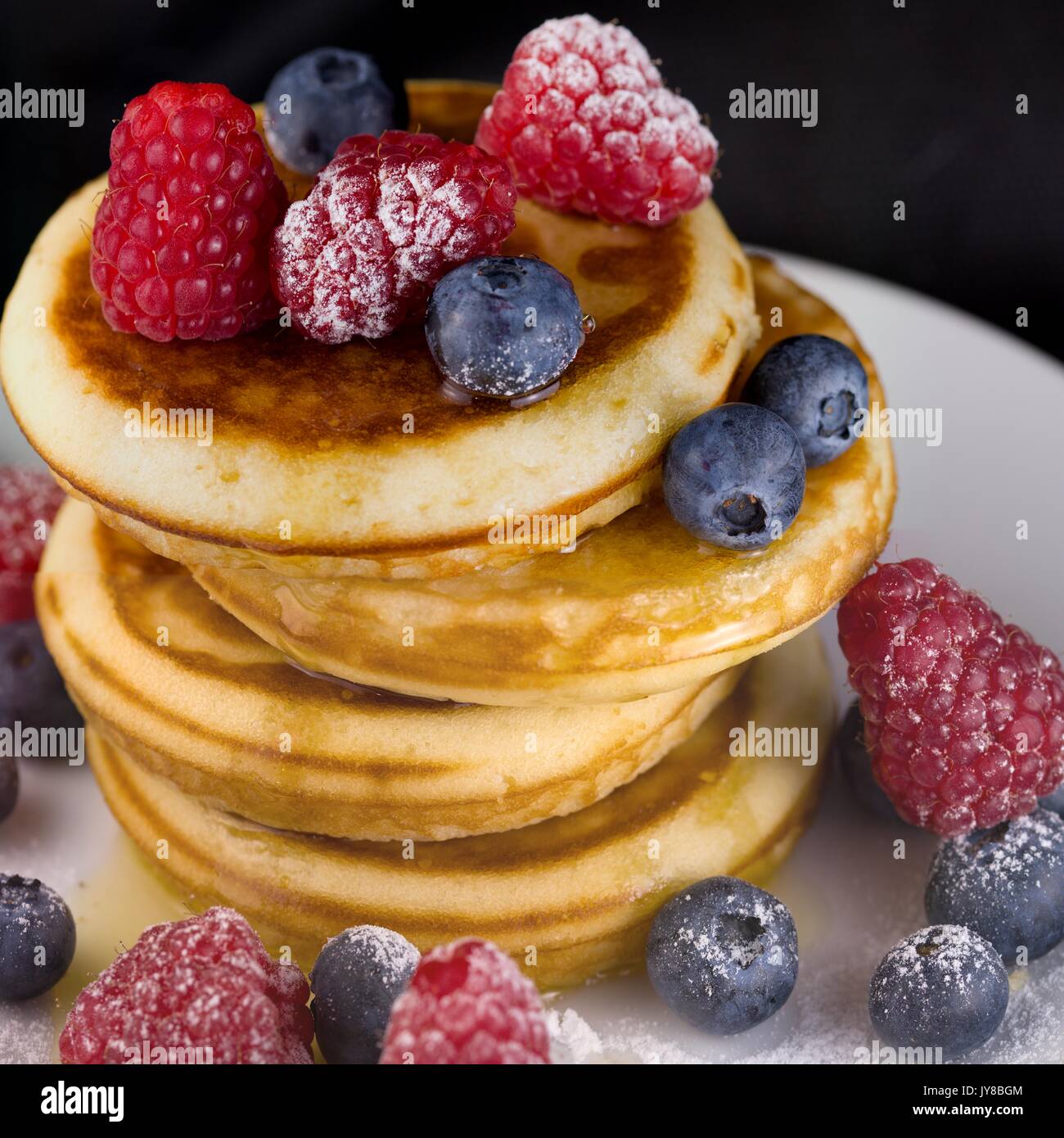 Pila di pancake con lamponi e mirtilli e miele il gocciolamento verso il basso il lato. Tenuta raccolto quadrato Foto Stock
