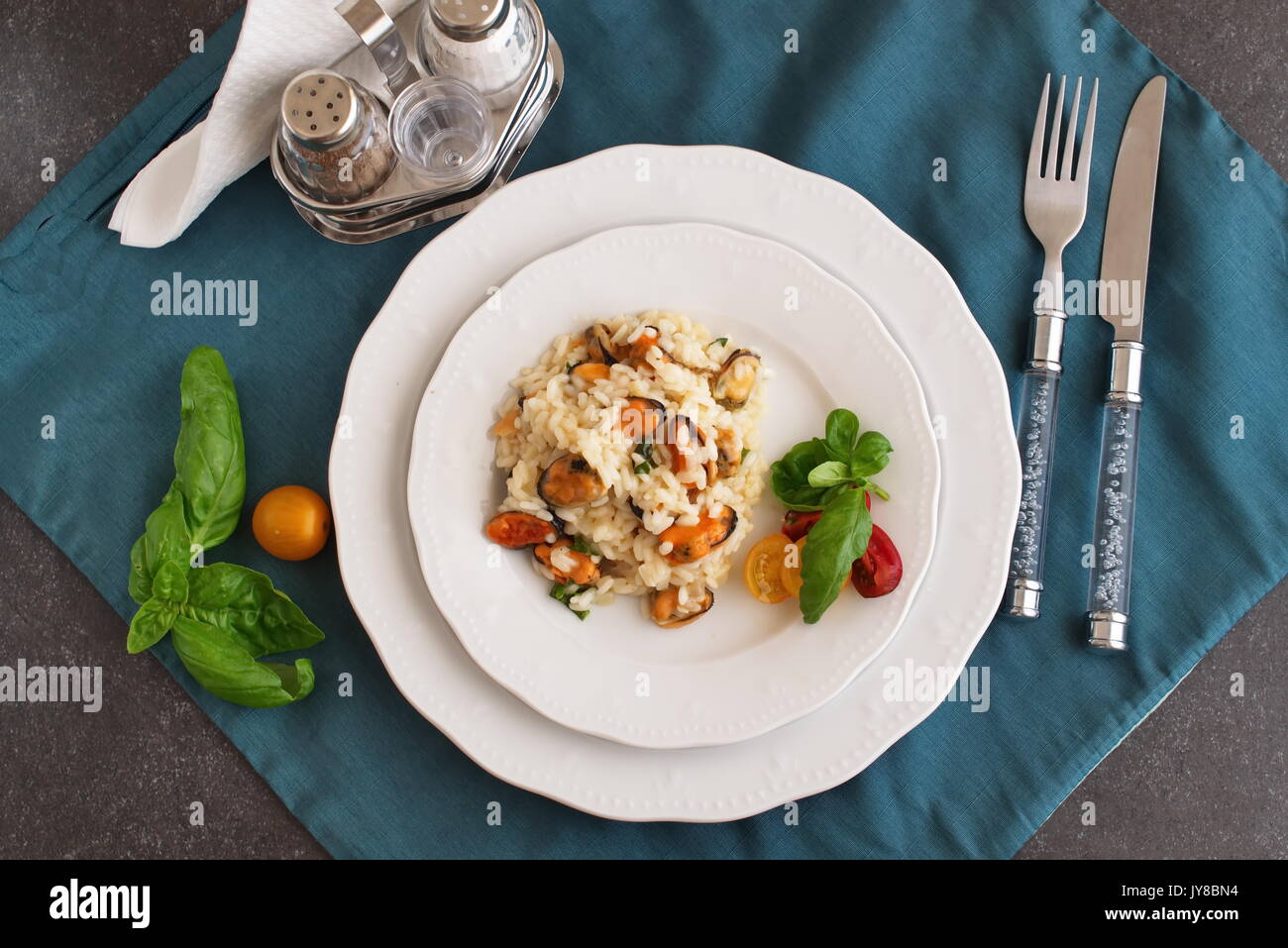 Risotto con le cozze su una piastra bianca con basilico, pomodori ciliegia su un panno verde. Mangiare sano concetto, Meditarranian stile di vita Foto Stock