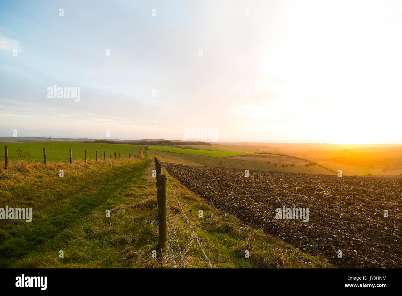 Ditchling Beacon, Sussex, Regno Unito. Un recinto e fango via filo verso l'orizzonte mentre il sole tramonta dietro i campi di rotolamento del Sussex. Foto Stock