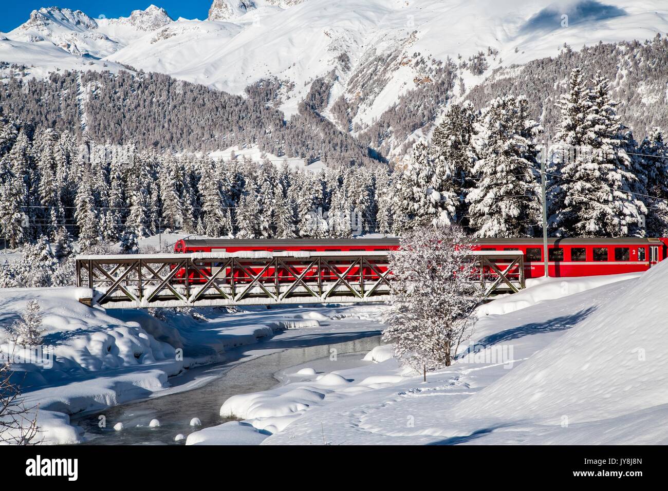 Il Trenino Rosso del Bernina attraversa un ruscello da un ponte. In Engadina, nel Cantone dei Grigioni, in Svizzera Europa Foto Stock