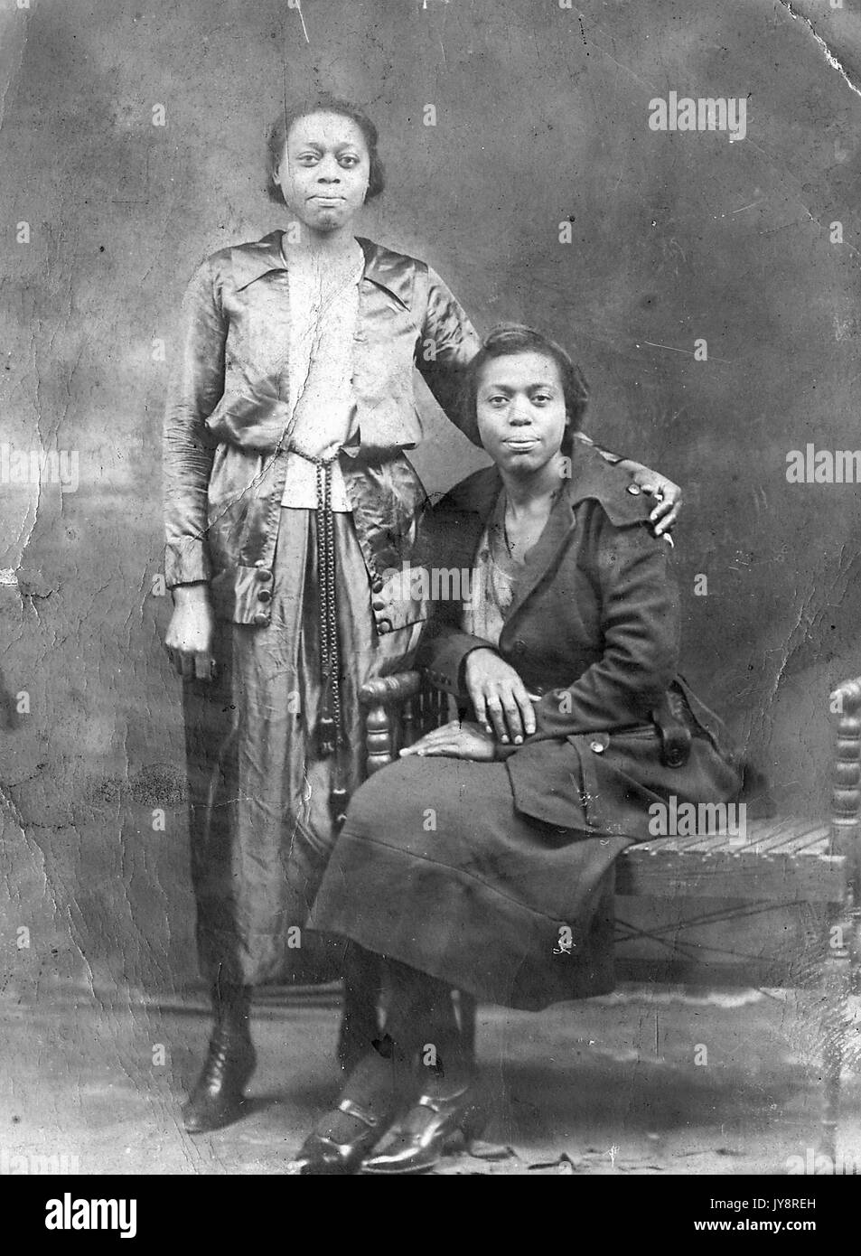 A piena lunghezza ritratto di due paesi africani le donne americane con espressioni neutre, uno in piedi indossando una camicetta, giacca e gonna, gli altri seduti su una panchina, indossando un pavimento scuro Lunghezza coat, 1915. Foto Stock