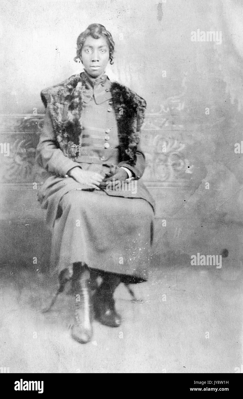 A piena lunghezza Ritratto di seduto americano africano donna, indossando una pelliccia scialle e abito scuro, con le mani appoggiate sul giro, 1915. Foto Stock