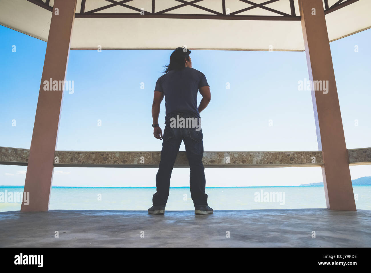 Un uomo asiatico stand trasformare il suo ritorno sotto il tetto vicino al mare Foto Stock