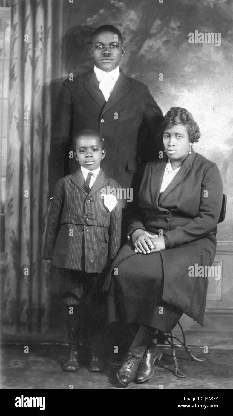 Famiglia americana africana in posa per una fotografia in studio con fondale dipinto, madre e figlio nella parte anteriore, padre nel retro, tutti indossano abiti formali, 1932. Foto Stock