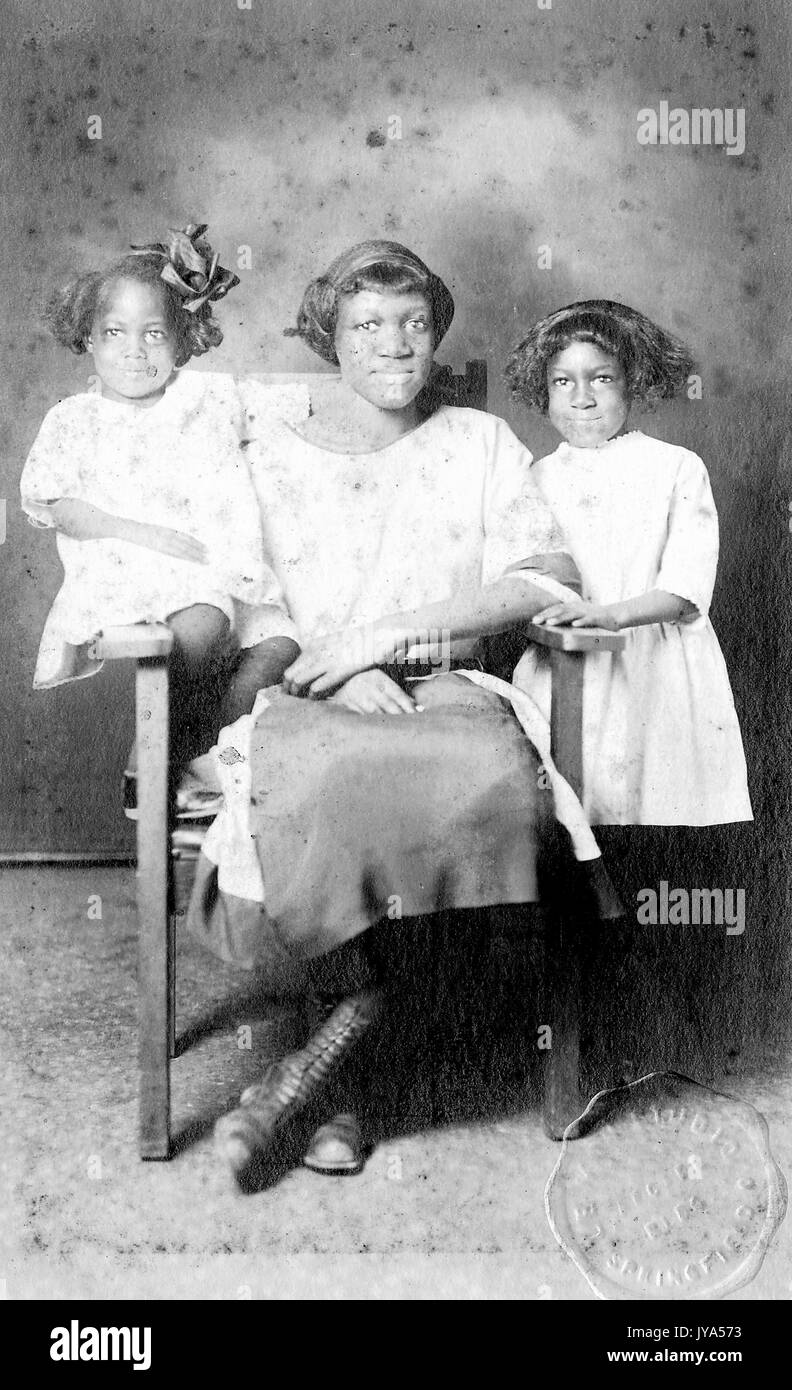 African-american madre in posa con le sue due figlie per un ritratto in studio seduto in una sedia, una figlia in piedi e appoggiata sulla sedia, la figlia più giovane seduto sul bordo della sedia, tutti indossano bianco, 1925. Foto Stock